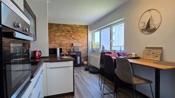 Eine moderne Küche mit Einbauofen, eine Essecke mit Holztisch und Stühlen sowie eine Wand mit Ziegelverkleidung.