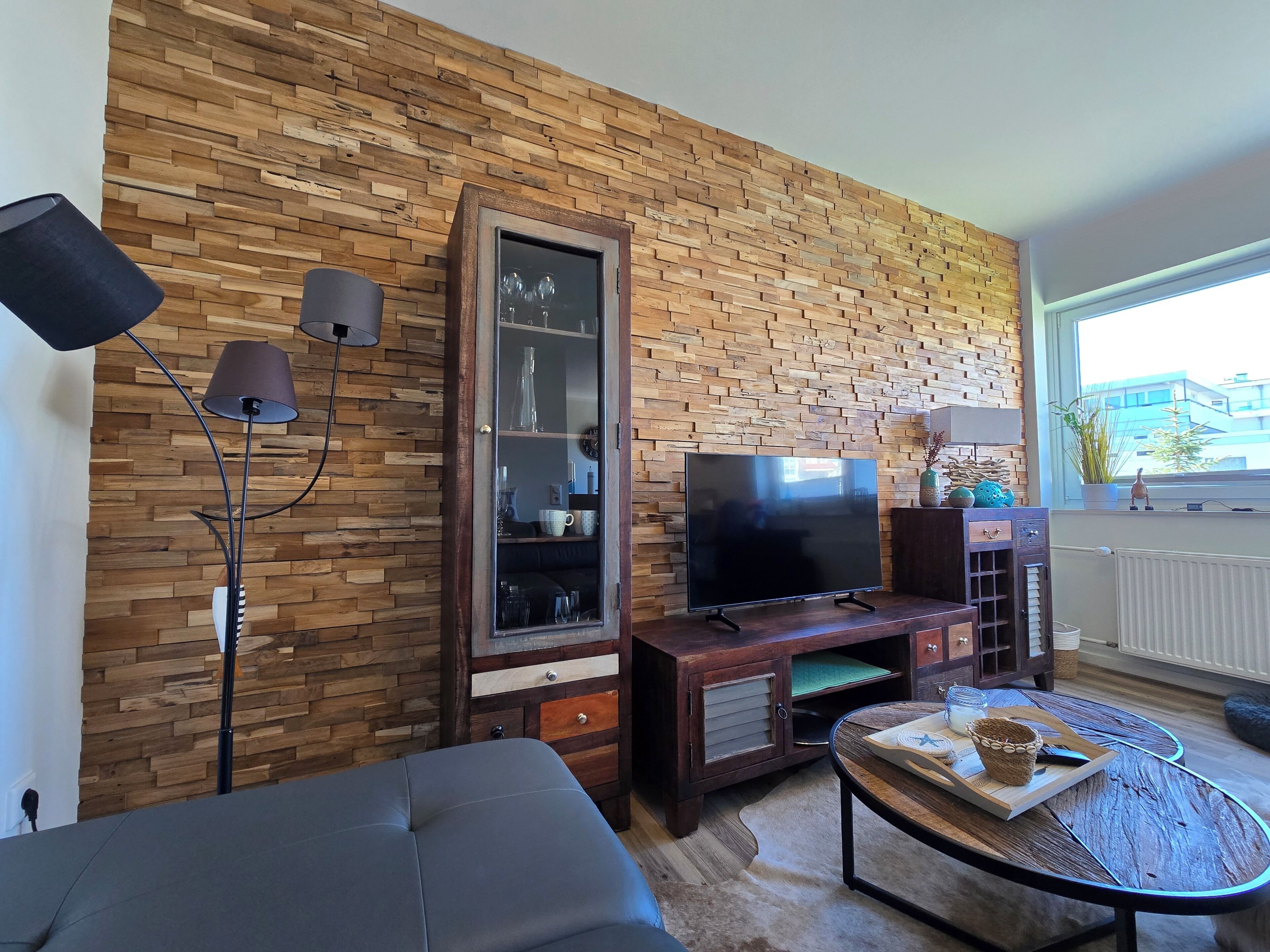 Ein Wohnzimmer mit Backsteinwand, Flachbildfernseher, dunklem Sofa, Couchtisch und Stehlampe.