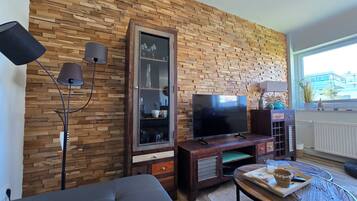 Ein Wohnzimmer mit Backsteinwand, Flachbildfernseher, dunklem Sofa, Couchtisch und Stehlampe.