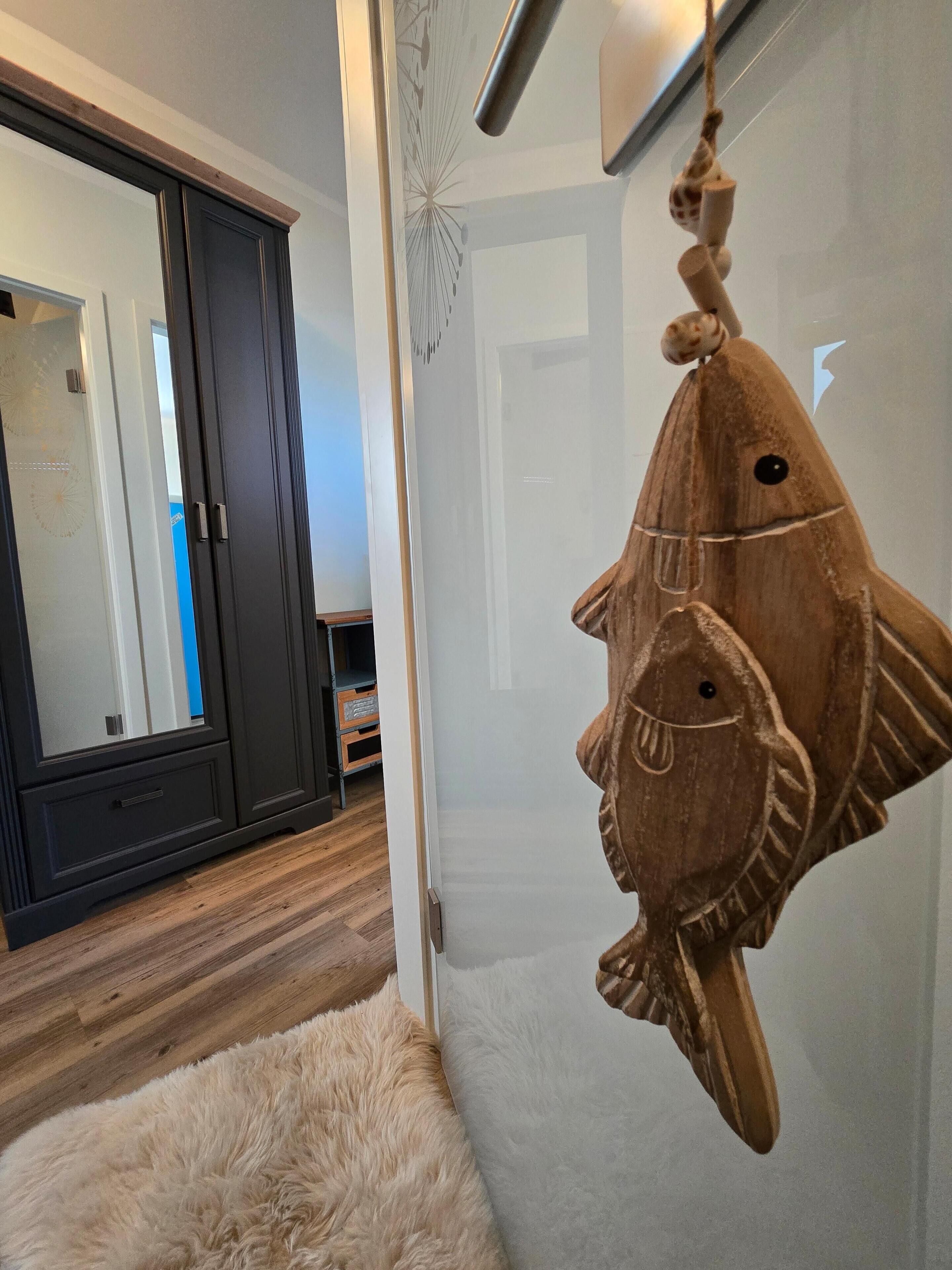 Ein Zimmer mit einem dunklen Holzschrank, einem weißen, flauschigen Teppich und einer Holz-Fischdekoration an der Wand.