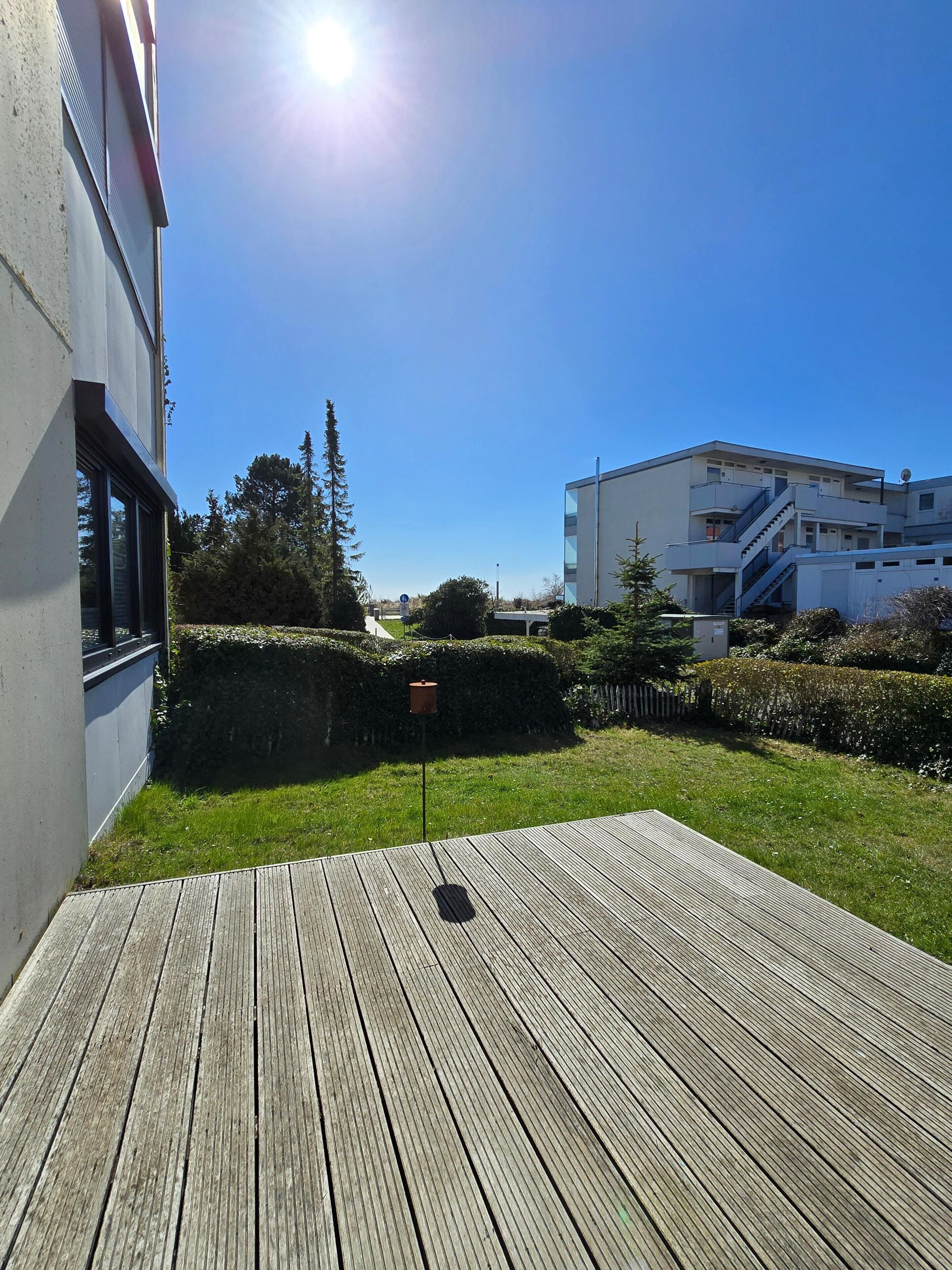 Eine Holzterrasse, ein Gebäude mit weißer Fassade und ein strahlend blauer Himmel.