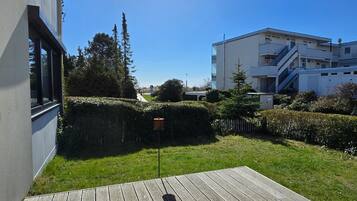 Eine Holzterrasse, ein Gebäude mit weißer Fassade und ein strahlend blauer Himmel.