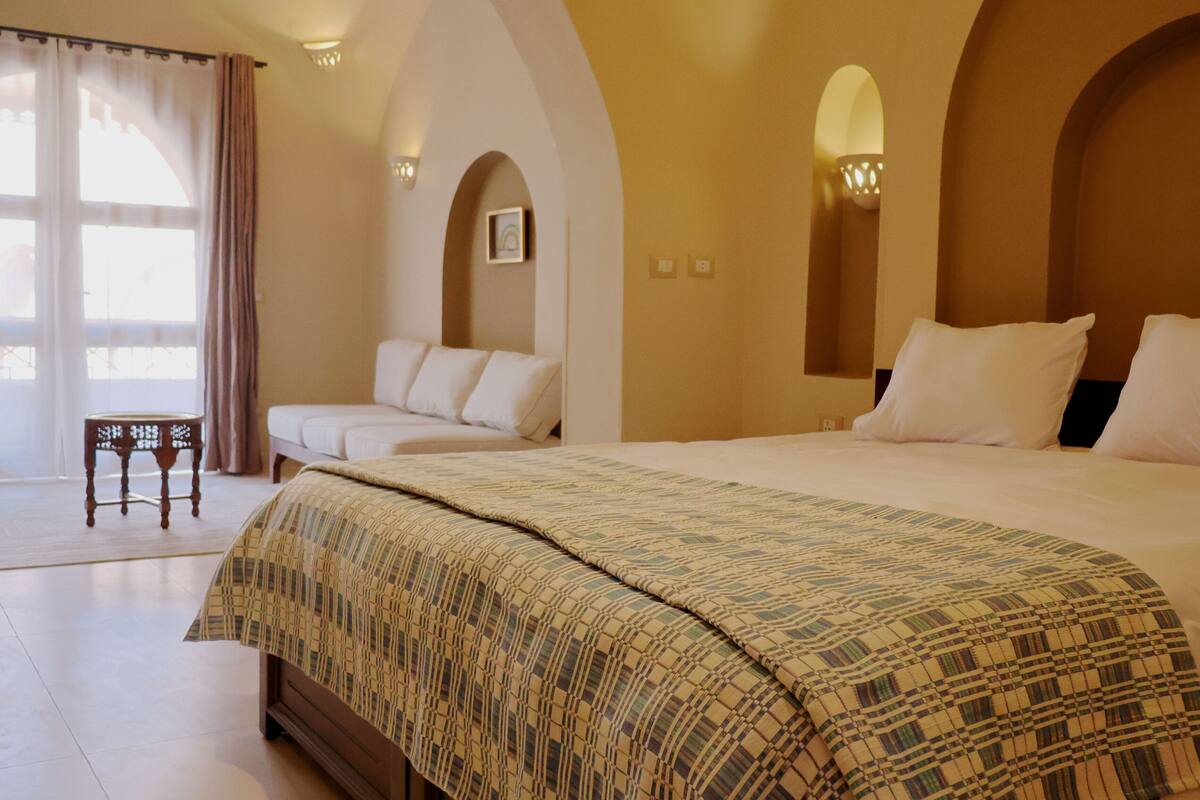Une chambre d’hôtel avec un grand lit, un canapé, une petite table et une vue sur l’extérieur.