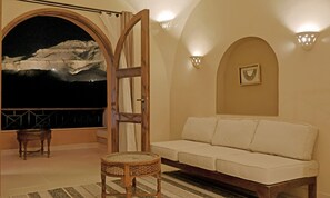 A room with a white sofa, a small round table, a large arched window with a painting, and wall sconces.