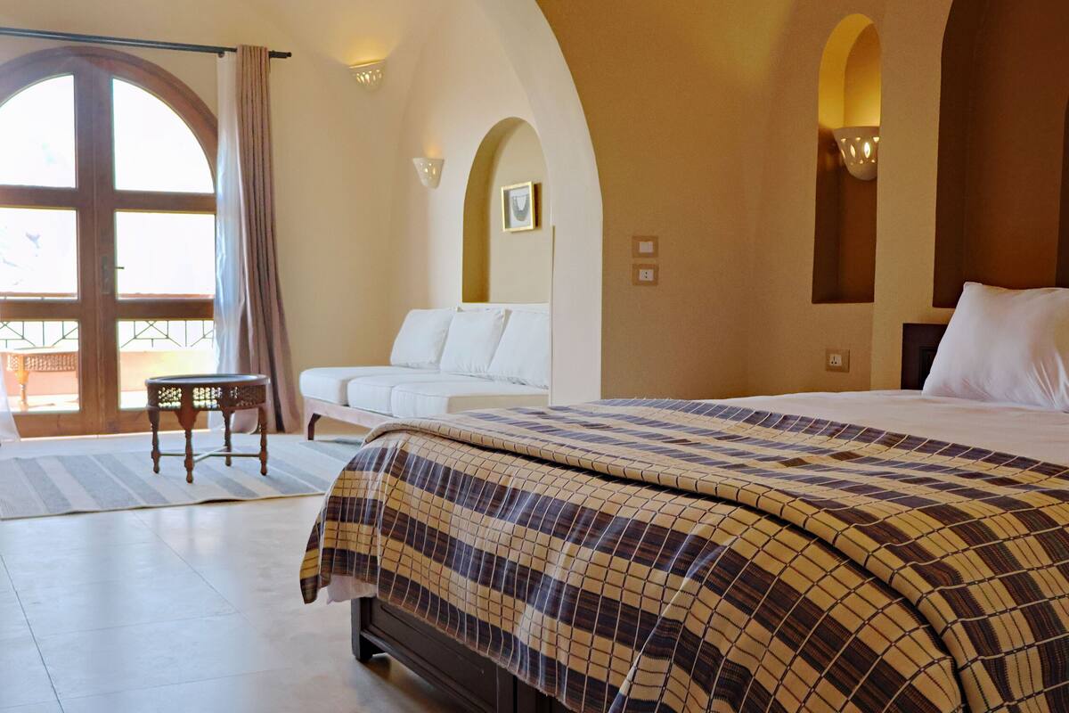 Une chambre d’hôtel avec un grand lit, un canapé, une petite table et un balcon avec vue.