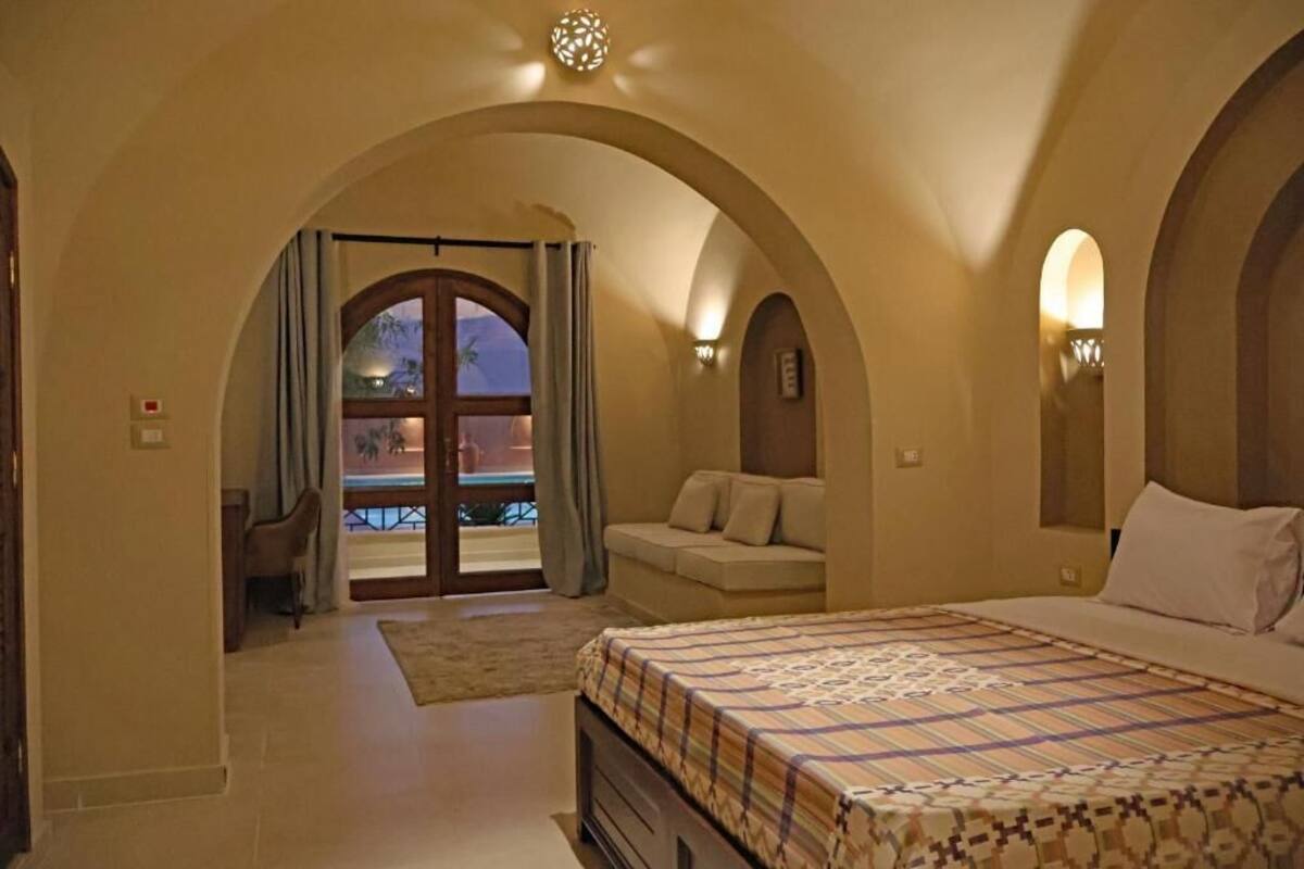 Une chambre à coucher avec un lit, un canapé et une vue sur l’extérieur, visible à travers une porte en arc de cercle.