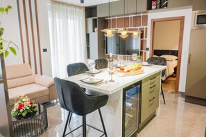 A modern kitchen with a central island, bar stools, and a dining area with a sofa and table. - Modern Apartment With Balcony in the Center (Drnis)