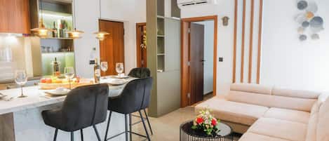 A modern kitchen with a dining area, a sofa, and a small side table with flowers.