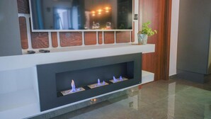Una sala de estar moderna con un televisor de pantalla plana montado en una pared blanca, una chimenea con llamas azules y una planta en maceta sobre una repisa.