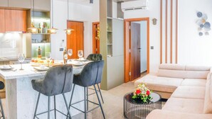 Una cocina moderna con taburetes de bar, una mesa de comedor preparada para dos personas y una sala de estar con sofá y una mesa de centro.