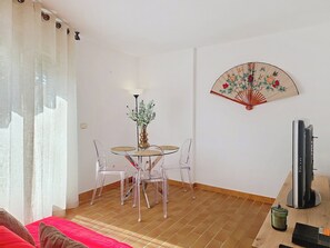 Ein Zimmer mit einem Esstisch, Stühlen, einer Pflanzvase, einem Ventilator und einem Fernseher.