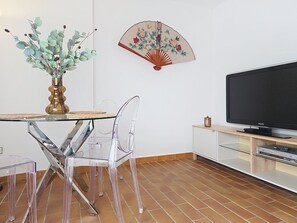 Ein modernes Wohnzimmer mit einem Glastisch, transparenten Stühlen, einem Fernseher und einem dekorativen Ventilator.
