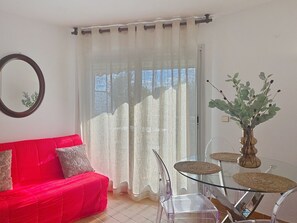 Ein Wohnzimmer mit einem roten Sofa, einem Glastisch mit gewebten Unterlagen, einem transparenten Stuhl und einer Vase mit Grünpflanzen.