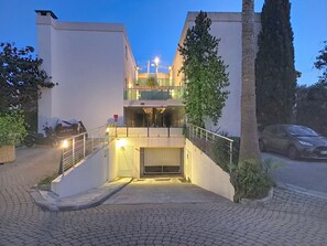 Ein mehrstöckiges Gebäude mit einer Treppe, die zu einem verschlossenen Eingang führt, ein Auto auf der Straße und ein Roller davor.