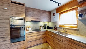 Eine moderne Küche mit Holzschränken, einem eingebauten Ofen und einem Fenster mit Vorhängen.