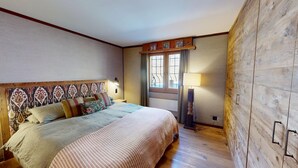 Ein Schlafzimmer mit einem Bett, einem Nachttisch, einer Lampe, einem Fenster mit Vorhängen und einer Holzwand.