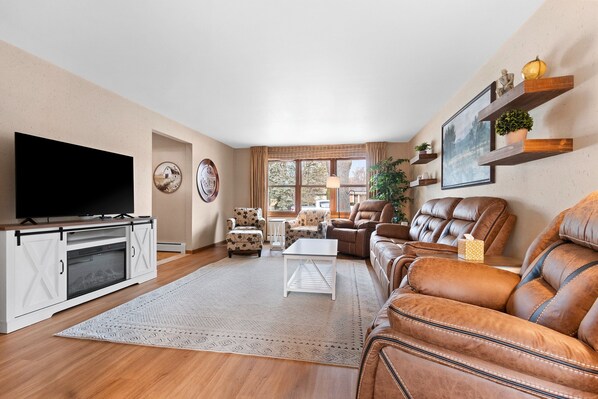 A living room with a flat-screen TV, a fireplace, leather sofas, a coffee table, and a large window.