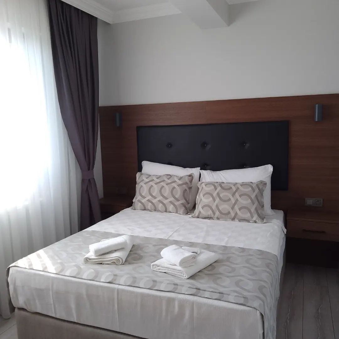 A hotel room with a bed, a headboard, and a window with curtains.