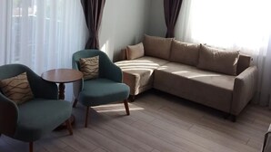 Ένα σαλόνι με έναν καναπέ, δύο πολυθρόνες, ένα μικρό τραπέζι και λεπτά, διάφανα κουρτίνες.