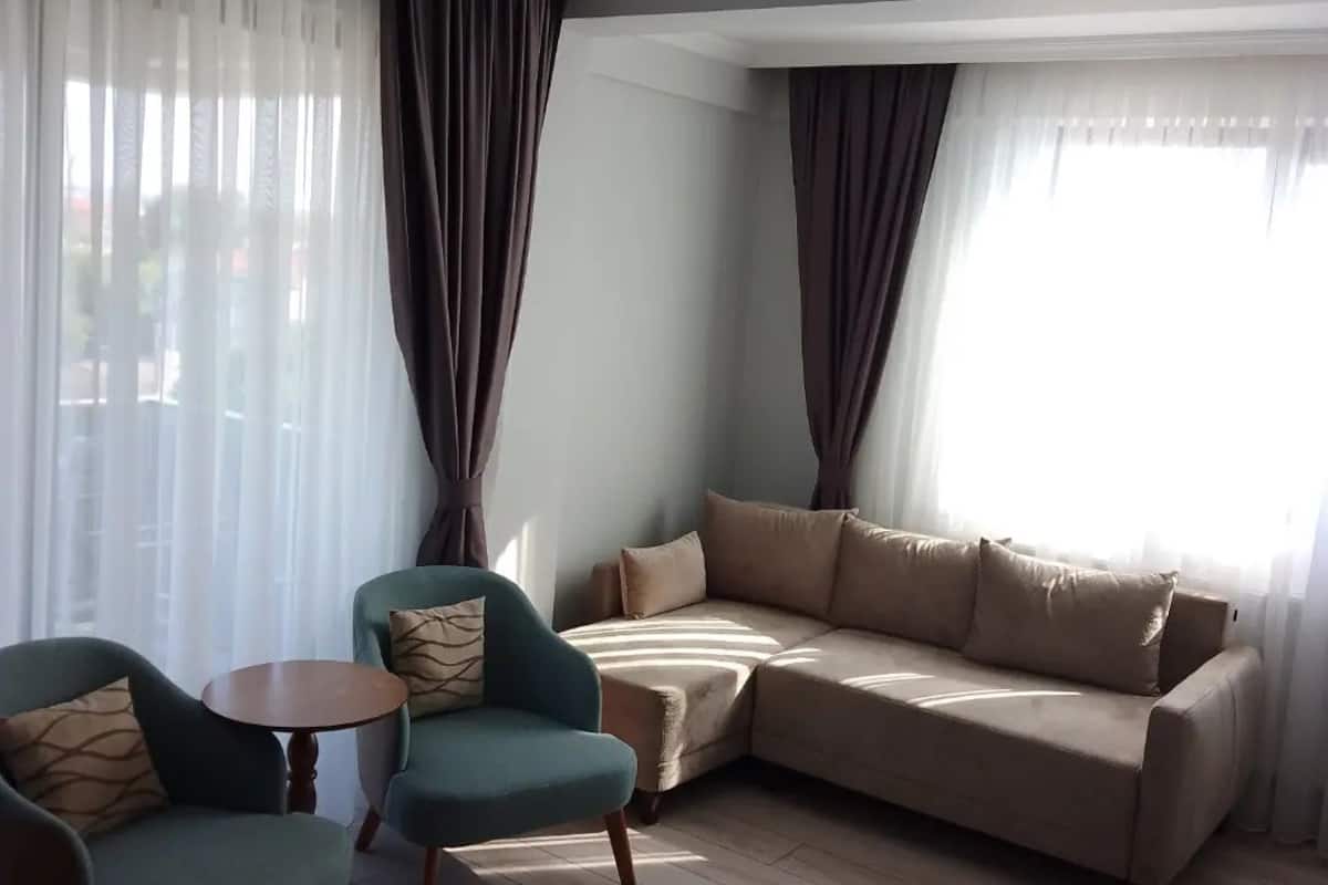 A living room with a sofa, two armchairs, a small table, and sheer curtains.