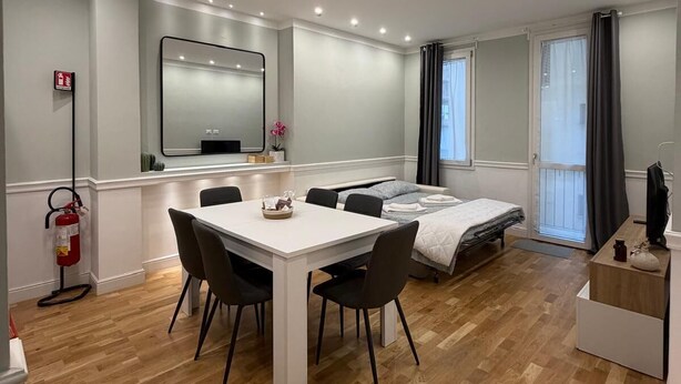 Een moderne kamer met een eettafel, stoelen, een bed, een televisie en een brandblusser.