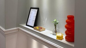 Een receptiegedeelte met een bord met daarop een welkomstboodschap, een plantje en een rode vaas op een plank.