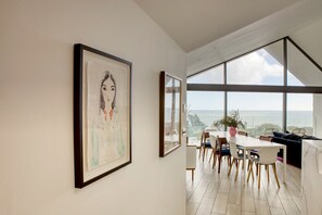 A modern dining area with a view of the sea, framed artwork on the wall, and a minimalist interior design. - 5 bedroom Modern beach house hot tub and sauna massive sea views beach access (Charmouth)