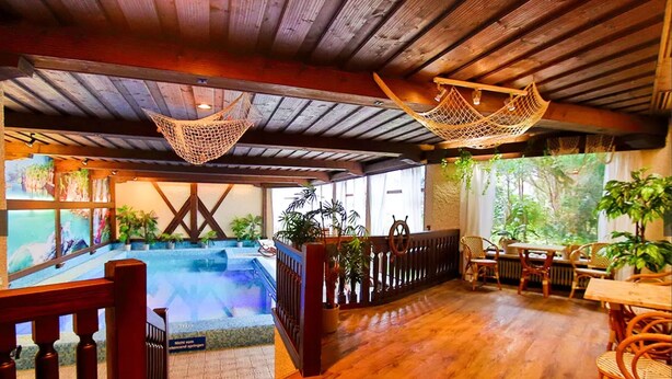 Una terraza de madera con piscina, mobiliario exterior y plantas en macetas.