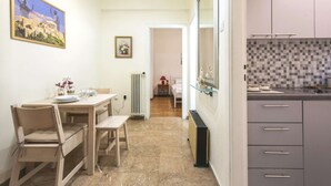 Uma sala de jantar com mesa e cadeiras, uma cozinha com armários, revestimento de azulejos e um corredor que dá para um quarto.