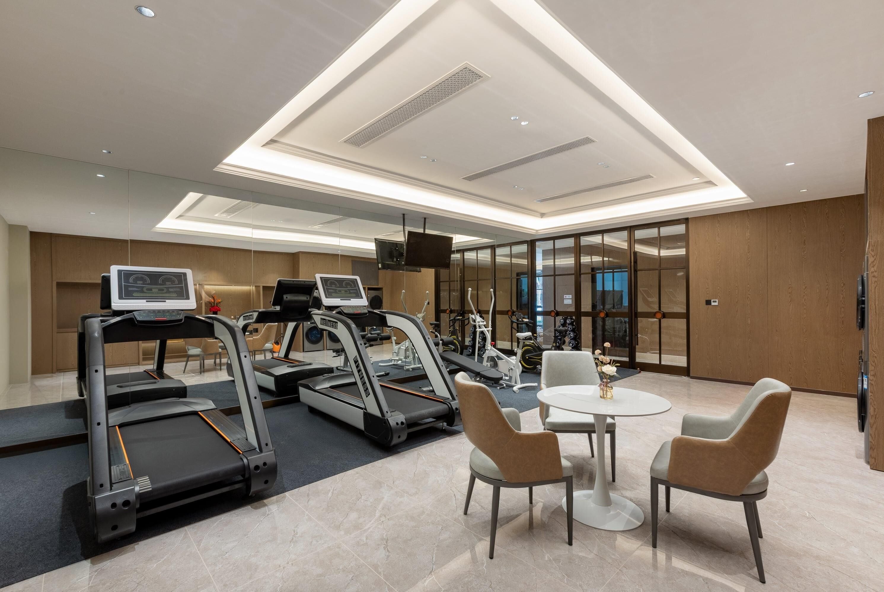 Un centre de remise en forme moderne équipé de tapis de course, d’appareils d’exercice et d’un espace détente avec une table et des chaises.