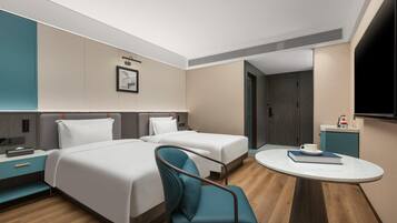 A hotel room with two beds, a desk, a chair, a round table, a TV, and a door.
