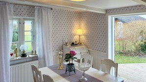 Un espace repas comprenant une table, des chaises, une lampe, un vase avec des fleurs et une vue sur l’extérieur.