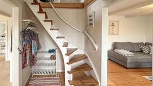 Un escalier avec des marches en bois et des murs blancs, menant à une pièce où se trouve un canapé gris et un tableau encadré au mur.