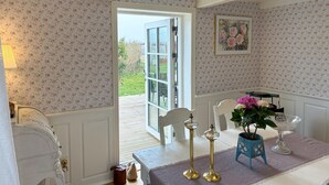 Une pièce avec un papier peint à motifs floraux, une table à manger avec des chaises, un petit chemin de table bleu et une plante en pot.