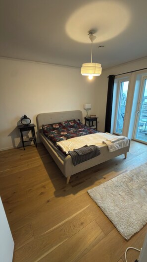 A bedroom with a bed, a bedside table, a lamp, a window, and a view of the outside.
