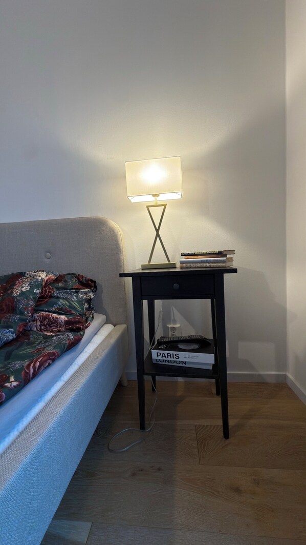 A bed with a floral bedspread, a bedside table with a lamp, and a book titled 'Paris'.