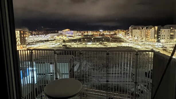 A balcony with a table and chairs, overlooking a cityscape at night. - Stylish luxury suite with magical golf views near the city (Örebro)