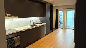 A modern kitchen with dark cabinetry, a wooden floor, and a view to the outside. - Stylish luxury suite with magical golf views near the city (Örebro)