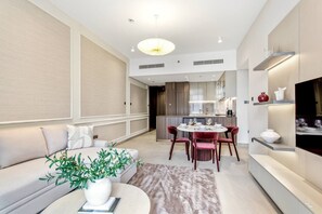 A modern living room with a sofa, dining table, and chairs, a potted plant, and a TV. - Cozy 1Bedroom w/ Rooftop Pool & Sauna in JVC (Dubai)