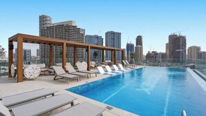 En pool på taket med solstolar och utsikt över stadens skyline.