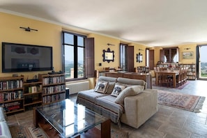 Ein Wohnzimmer mit einer Couch, einem Couchtisch, Bücherregalen, einem Fernseher und einem Essbereich mit Stühlen und einem Tisch.