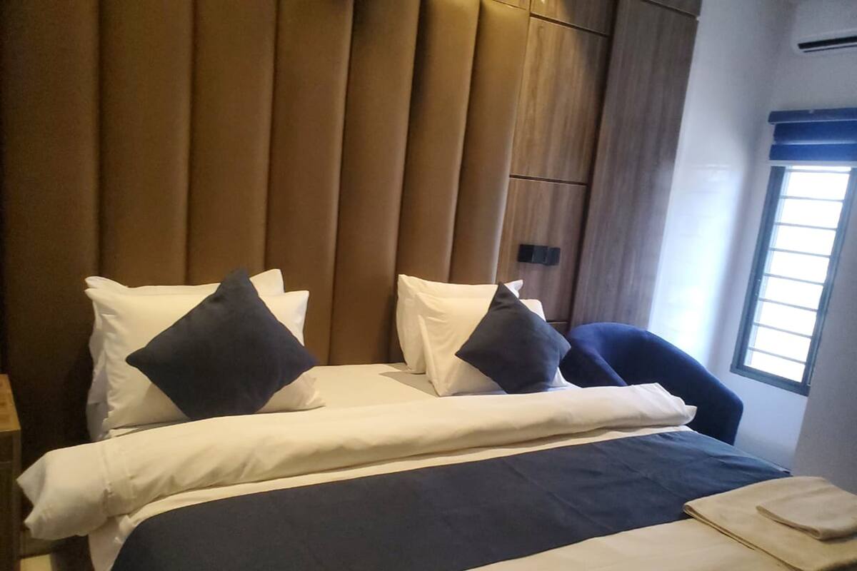 A hotel room with a bed, pillows, a chair, and a window.