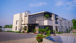 A modern building with a large entrance, a fountain, and a paved area with plants.