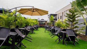 A patio with rows of black chairs and tables, a yellow umbrella, and green artificial grass.