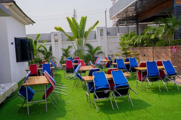 A classroom with desks and chairs arranged in rows, surrounded by a green lawn and palm trees.