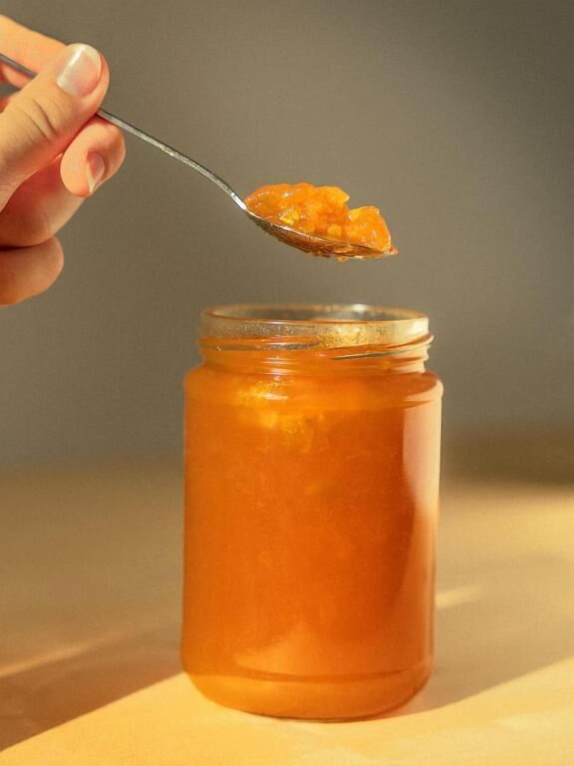 A hand holding a spoon over a jar of orange substance.