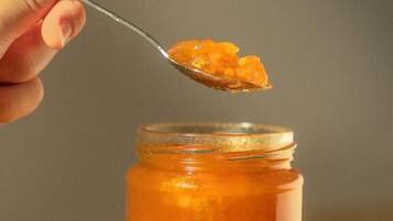 A hand holding a spoon over a jar of orange substance.