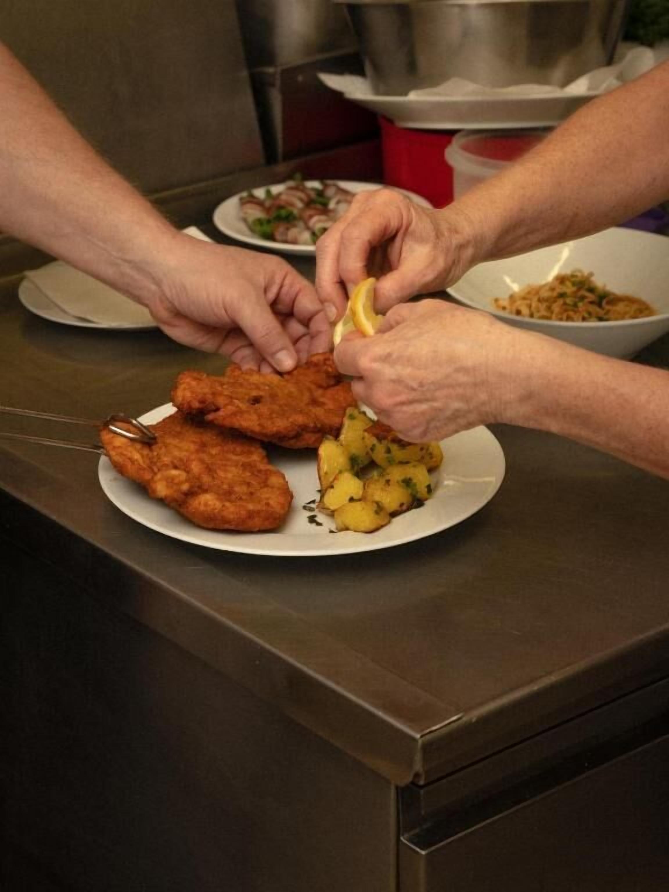 A person serving food, including a breaded cutlet and potatoes, on a plate.