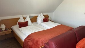 A single bed with a wooden headboard, white bedding, and red accents. There is a nightstand with a lamp and a power outlet. A red leather sofa is positioned at the foot of the bed. - Gästehaus Freitag  (Sankt Georgen im Lavanttal)