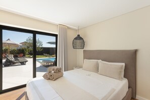 Una habitación de hotel con una cama grande, vista a una piscina y una lámpara colgante.